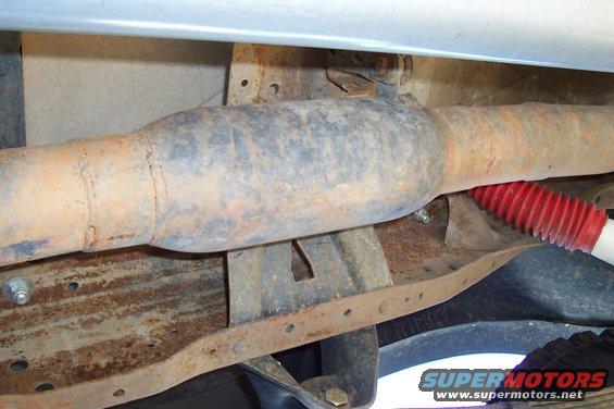 underbody shot of rusty exhaust pipe and red shock absorber boot