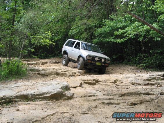Silver 1995 Nissan Pathfinder navigating a rocky trail with trees in the background