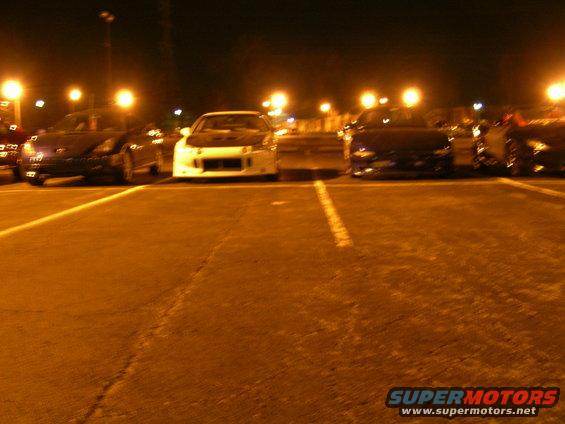 Several sports cars parked in a lot at night under streetlights