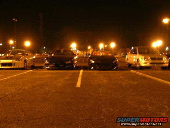 Several cars parked in a lot at night under streetlights