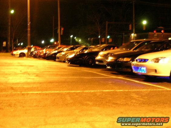 Several cars parked in a line at night, one has blue underglow