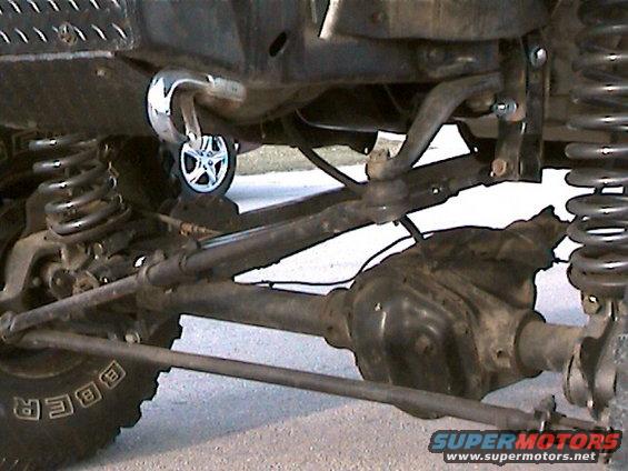 Truck undercarriage with suspension components, differential, and tire visible. A chrome tow hook is attached to the frame