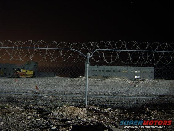 Barbed wire fence in front of industrial buildings at night