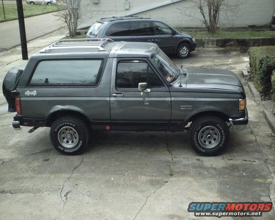 Gray 1987 Ford Bronco parked on concrete, side view, with a spare tire on the rear