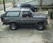 1987 Ford Bronco - A gray 1987 Ford Bronco is parked on a concrete driveway next to a dark minivan.