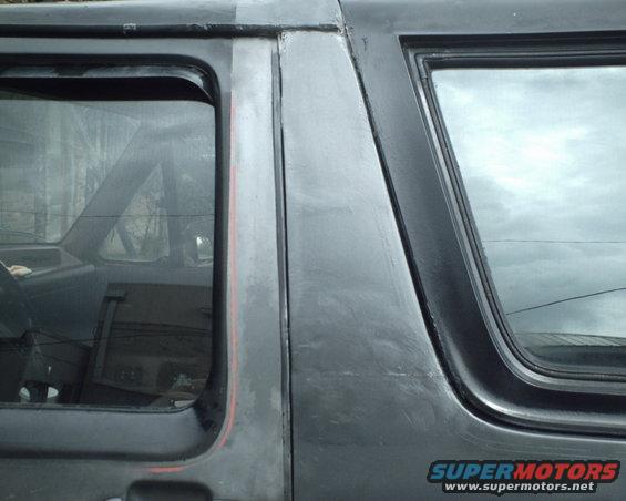 Side view of a dark SUV's rear door and window with a red stripe detail