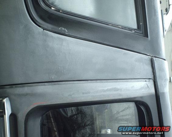 Close-up of a dark gray vehicle body panel with window trim and a SuperMotors watermark