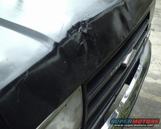 Front grille and dented hood of a black 1987 Ford Bronco