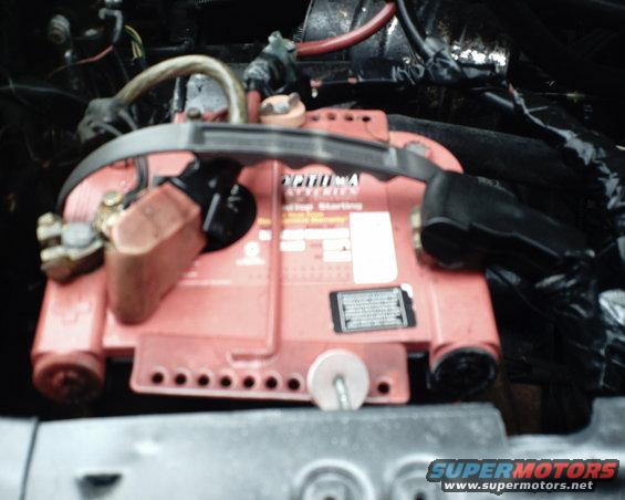 Red Optima car battery with black terminals and cables, top view