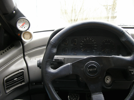Car interior with a black steering wheel and two gauges visible on the left