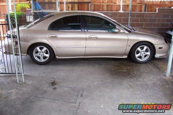 Tan sedan parked under a covered area, side view. The car has tinted windows and alloy wheels