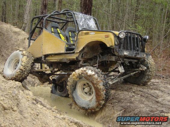 Yellow off-road buggy with roll cage navigating muddy terrain