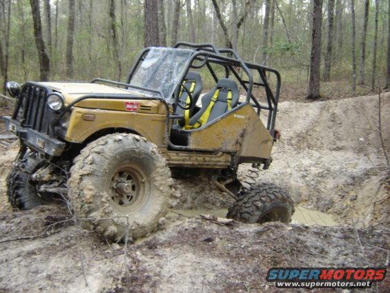 Yellow off-road vehicle with a roll cage stuck in mud, front-left tire deep in a rut