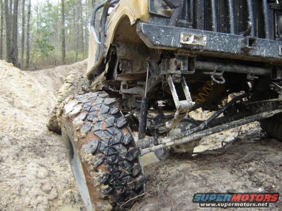Off-road vehicle's front suspension and large tire covered in mud on a dirt track
