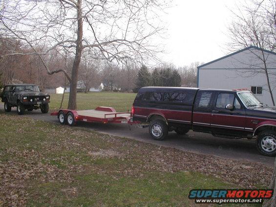 Dark green 1978 Ford Bronco on a trailer being towed by a red and black pickup truck