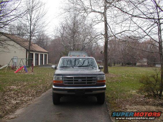 Front view of a dark-colored Ford F-Series truck, possibly a 1992 model, parked in a driveway. Another vehicle is visible behind it