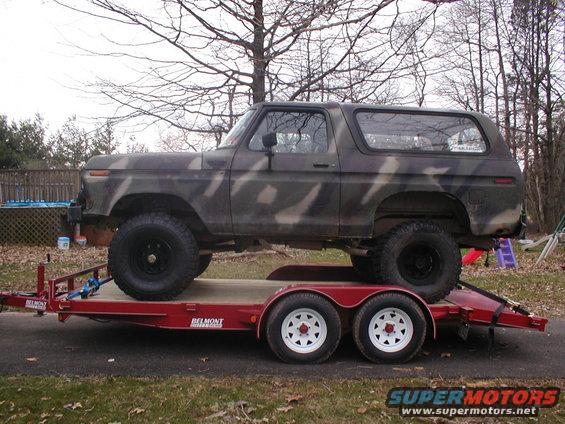 Camouflaged Ford Bronco on a red trailer, side view