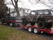 1979 Ford Bronco - A camouflaged 1979 Ford Bronco is transported on a trailer, pulled by a pickup truck.