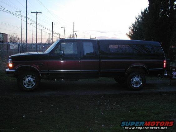 Two-tone red and black pickup truck with a black camper shell, seen from the side