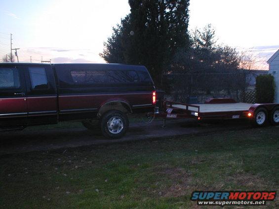 Side view of a red and black pickup truck towing a flatbed trailer