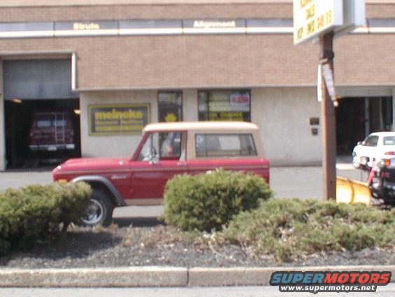 Red 1979 Ford Bronco with tan top parked outside a Meineke