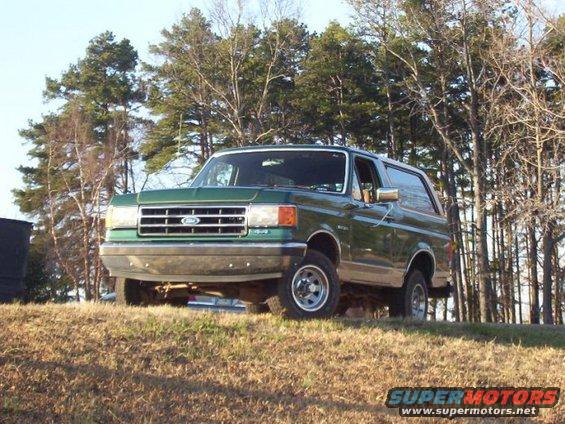 Green Ford Bronco parked on a grassy hill with trees behind it