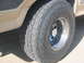 1986 Ford Bronco - A close-up view of a Nitto Terra Grappler tire mounted on a chrome wheel, with a portion of the vehicle's body visible.