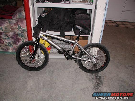 Silver BMX bicycle with black handlebars and seat, parked indoors on a concrete floor