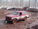 2000 Chevrolet Tahoe - A red and white Ford Bronco navigates a muddy terrain with trees and snow in the background.