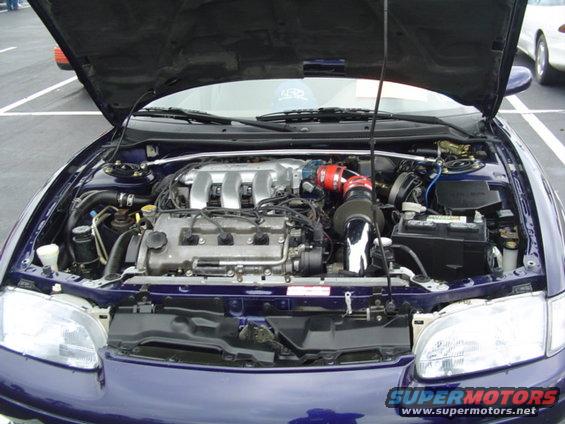 Open hood of dark blue Mazda MX-6 showing V6 engine with red intake and strut brace