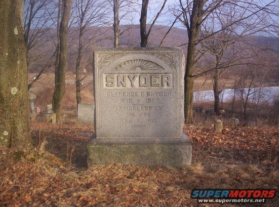 Gravestone for Snyder family in a cemetery with trees and a lake in the background