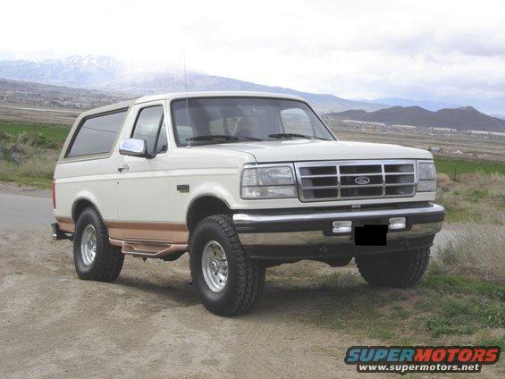 White Ford Bronco with brown trim, lifted, on dirt road, mountains in background