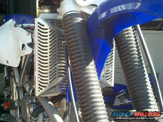 Motorcycle radiator guard and ribbed front fork boots on a blue and white dirt bike