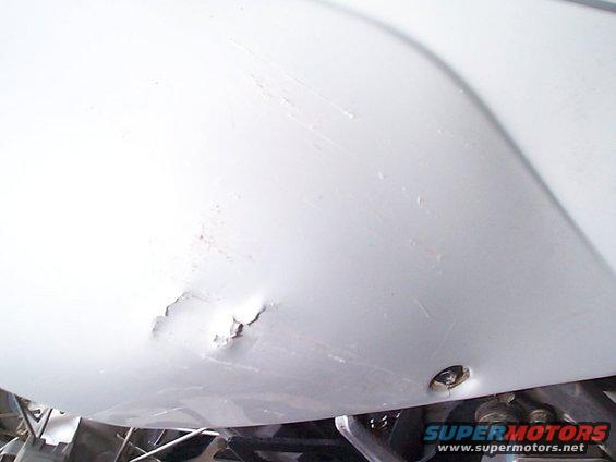 White motorcycle fender with a dent and scratches, showing a screw hole