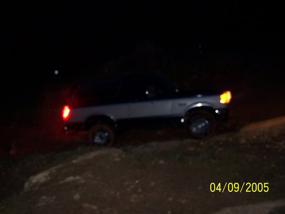 Ford Bronco parked on dirt at night, headlights and taillights on