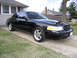 1999 Ford Crown Victoria - A black sedan is parked on a concrete driveway next to a grassy lawn.