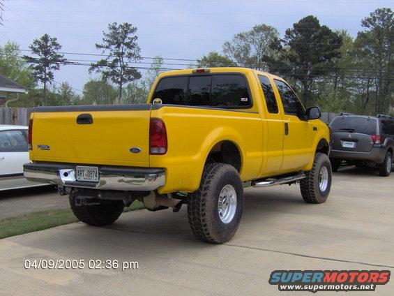 Yellow 1999 Ford F-250 pickup truck parked in driveway, rear view. Another SUV is parked behind it