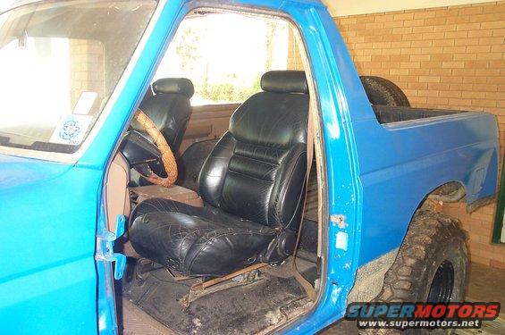 Blue pickup truck interior with black leather seats and a tan steering wheel. The driver's side door is open