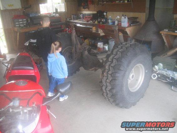 Off-road vehicle chassis with large tires, red motorcycle in foreground