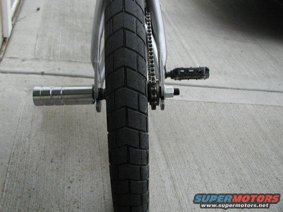 Bicycle rear wheel with knobby tire, chain, and pedal on concrete