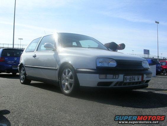 White VW Golf Mk3 with a person leaning over the hood, parked next to a blue VW Golf. License plate N-694 W is visible