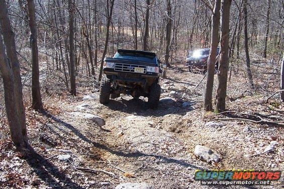 Black SUV with lifted suspension on a rocky trail, another vehicle behind