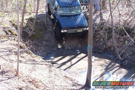 Black SUV driving down a muddy hill with trees around