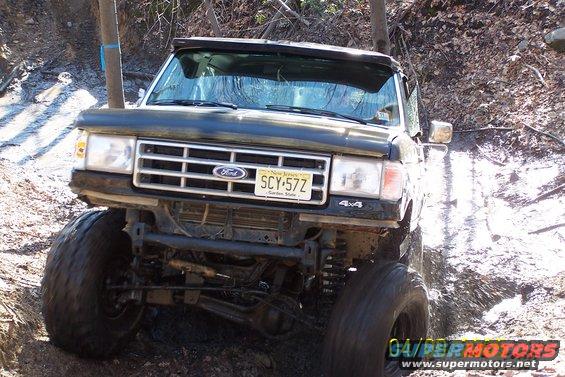 Black Ford truck with large tires on a muddy trail
