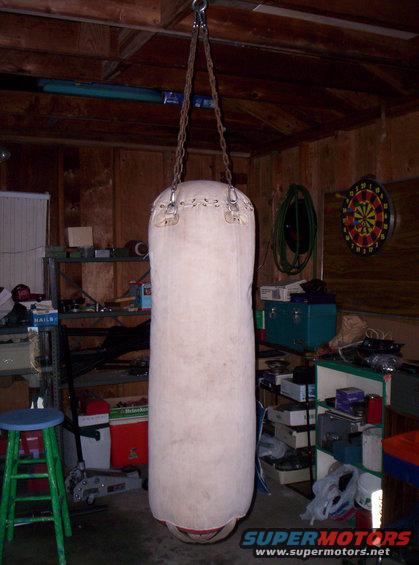 Punching bag hanging from chains in a cluttered garage with shelves, tools, and a dartboard