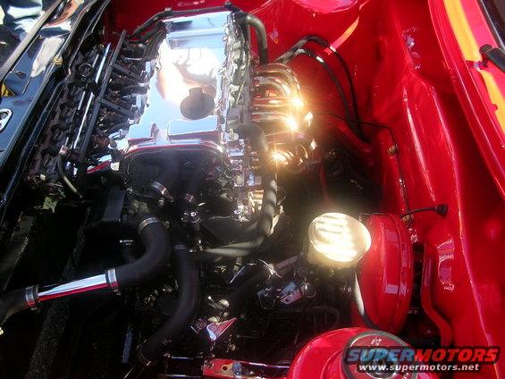 Engine bay with chrome intake manifold and red painted inner fenders. A round headlight is visible