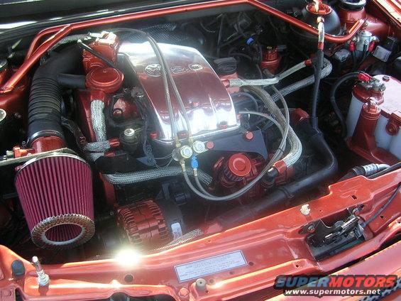 Engine bay with a red aftermarket air filter and chrome valve cover with "2.0" visible