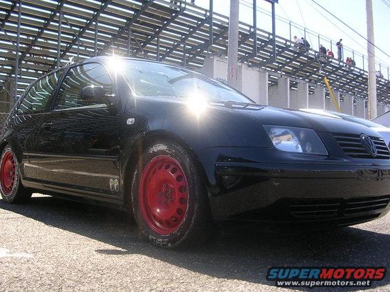 Black Volkswagen Jetta with red steel wheels parked near bleachers