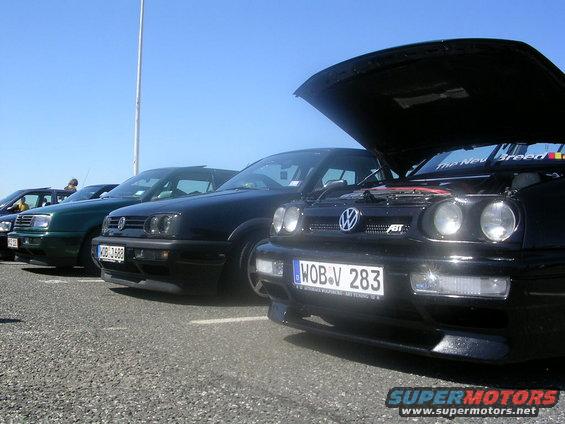 Several Volkswagen Golfs parked in a lot, one with its hood open showing the engine