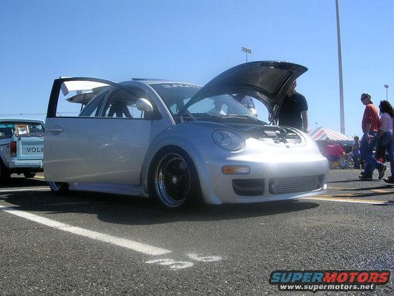 Silver Volkswagen Beetle with hood and driver door open, parked next to a light blue pickup truck